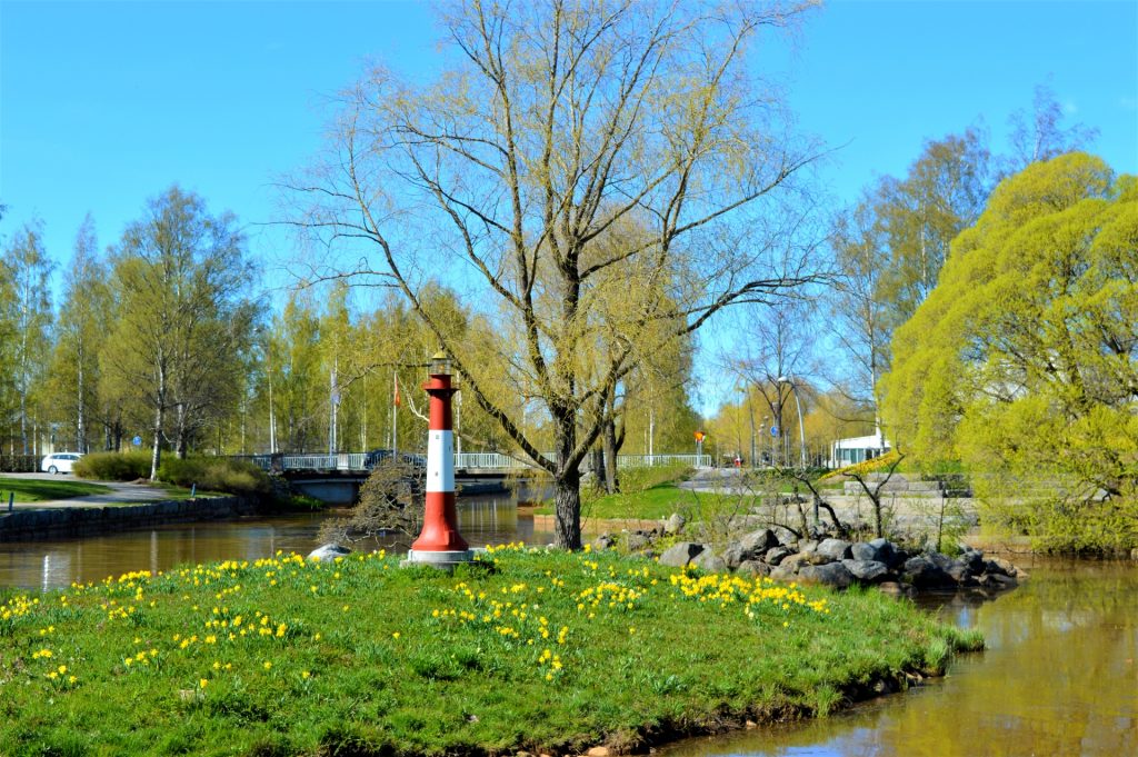 Kesä on tullut Kokkolaan ja kaupunginsalmi Suntissa sijaitsevassa Eskonsaaressa pienen koristemajakan ympärillä kukkivat voikukat. Lehdet ovat puhkeamassa puihin ja Sunti ympäröi pientä saarta.