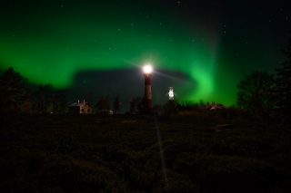 Upeat vihreät revontulet loimuavat Tankarin yllä tähtitaivaalla. Tankarin puna-valkoisen majakan valo loistaa yössä kirkkaana. Kuvaaja Hannu Tikkanen.